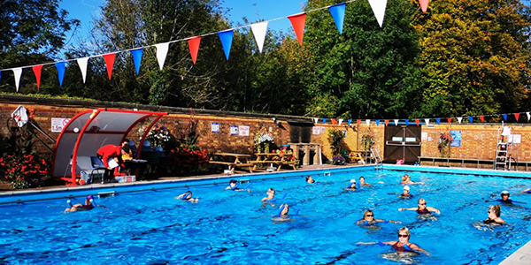 People in outdoor pool taking part in water aerobics class on a summer's day